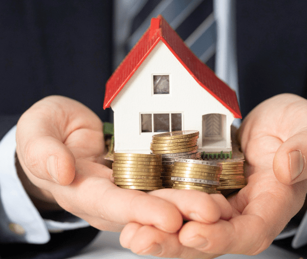 A person in a business suit holds a small model of a house resting on stacked coins, symbolizing real estate investment or homeownership savings. A person in a business suit holds a small model of a house resting on stacked coins, symbolizing real estate investment or homeownership savings.